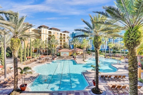 A hotel pool area with palm trees, lounge chairs, and a building in the background. - 3BR Floridays Suite on I-Drive (Orlando)