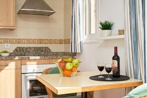 Una cocina con una mesa de comedor, un cuenco de fruta, dos copas de vino y una botella de vino.