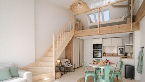 Een modern loft appartement met een houten wenteltrap, een eethoek met een ronde tafel en stoelen, een kitchenette en een zithoek met een bank.