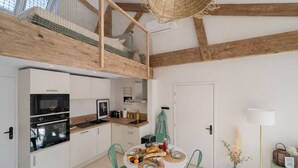 Een compacte keuken met moderne apparatuur, een eethoek met een ronde tafel, en een slaapverdieping met een houten plafond.