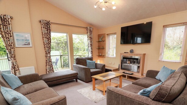 A living room with a sofa, armchair, and a flat-screen TV mounted on the wall. - L21 Coastal Kippford (Dalbeattie)