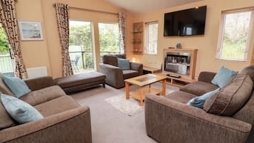 A living room with a sofa, armchair, and a flat-screen TV mounted on the wall.