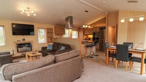 Ein gemütlicher Wohnbereich mit Sofa, Fernseher, Kamin, Küchenzeile und Esstisch.