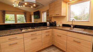 A modern kitchen with granite countertops, wooden cabinets, a stainless steel range hood, and a window with blinds.