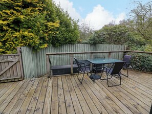 Une terrasse en bois avec une table et des chaises, entourée d’une clôture en bois et de verdure.