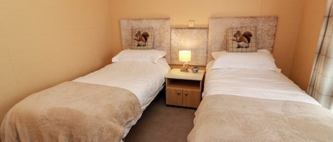 Ett hotellrum med två separata sängar, ett nattduksbord med en lampa och en vägghylla med dekorativa föremål.