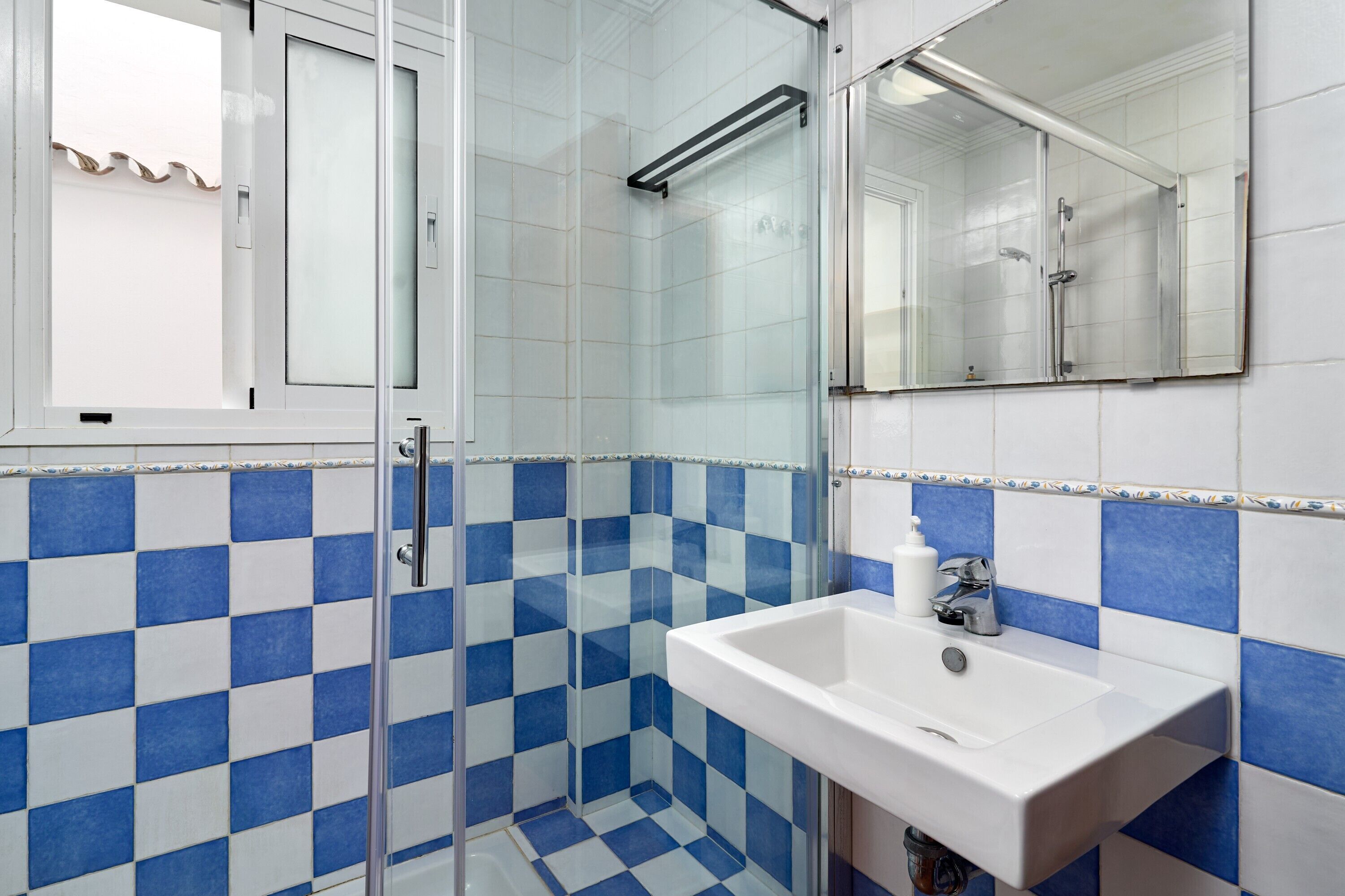 Une salle de bain avec une douche à parois de verre, un lavabo blanc et des carreaux bleus et blancs formant un motif à carreaux.
