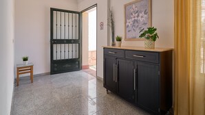 A hallway with a black cabinet, a small wooden stool with a plant, a framed floral artwork, and a door with a metal gate. - Apartment '1D - 2 bedrooms 4-6 people' with shared pool, Wi-Fi and air conditioning (Nerja)