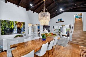 A modern dining area with a wooden table, white chairs, a chandelier, and artwork on the walls. - MIAMI EUROPEAN SPA LIKE HOME 10 MINUTES TO THE BEACH WALK TO GOLF COURSES (Miami Shores)