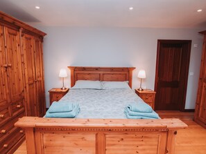 Ein Schlafzimmer mit einem hölzernen Bett, zwei Nachttischen mit Lampen, einer Holzbank und einem Kleiderschrank.
