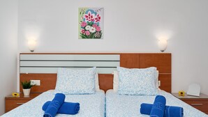 Une chambre d’hôtel avec un lit, deux tables de chevet, un luminaire fixé au mur et une œuvre d’art à motifs floraux.