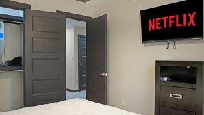 Quarto de hotel com cama, guarda-roupa, televisão na parede e porta de acesso a outro cômodo.