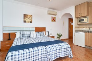 A bedroom with a bed, bedside tables, a nightstand, a wall-mounted air conditioner, a microwave, and a small kitchen area with a refrigerator. - Studio '2C with Balcony, Mountain View, Wi-Fi & Air Conditioning' (Nerja)