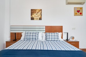 A neatly made bed with a checkered bedspread, a wooden headboard, a bedside table with a lamp, and a wall art piece above the bed. - Studio '2C with Balcony, Mountain View, Wi-Fi & Air Conditioning' (Nerja)