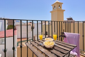 A balcony with a table set for two, two glasses of orange juice, a bowl of chips, and a chair with a purple towel. - Studio '2C with Balcony, Mountain View, Wi-Fi & Air Conditioning' (Nerja)