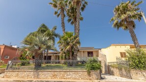 A residential area with palm trees, a stone wall, and houses with visible windows and doors. - APARTMENT IN VILLA MANZO (Terra Rossa)