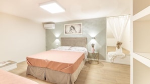 A bedroom with a bed, a bedside table with a lamp, a wall-mounted air conditioner, and a framed picture above the bed. - APARTMENT IN VILLA MANZO (Terra Rossa)