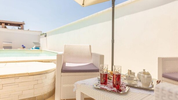 A poolside area with a wicker chair, a table with a tray of drinks, and a white wall. - APARTMENT IN VILLA MANZO (Terra Rossa)