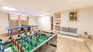 A room with a foosball table, a ping pong table, a sofa, and a shelf with decorative items. - APARTMENT IN VILLA MANZO (Terra Rossa)