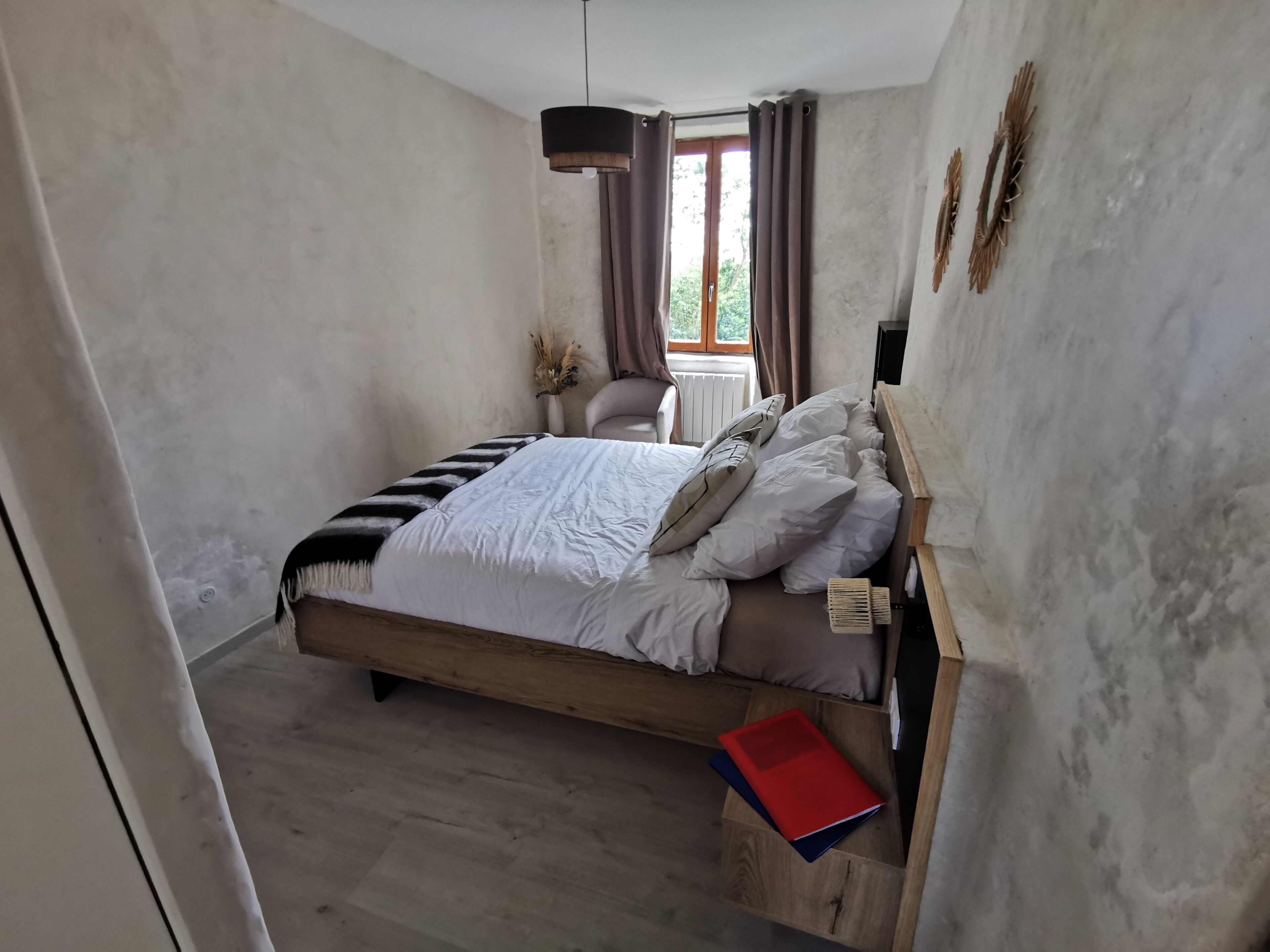 Une chambre à coucher avec un lit en bois, une table de chevet, une fenêtre avec des rideaux et un radiateur fixé au mur.