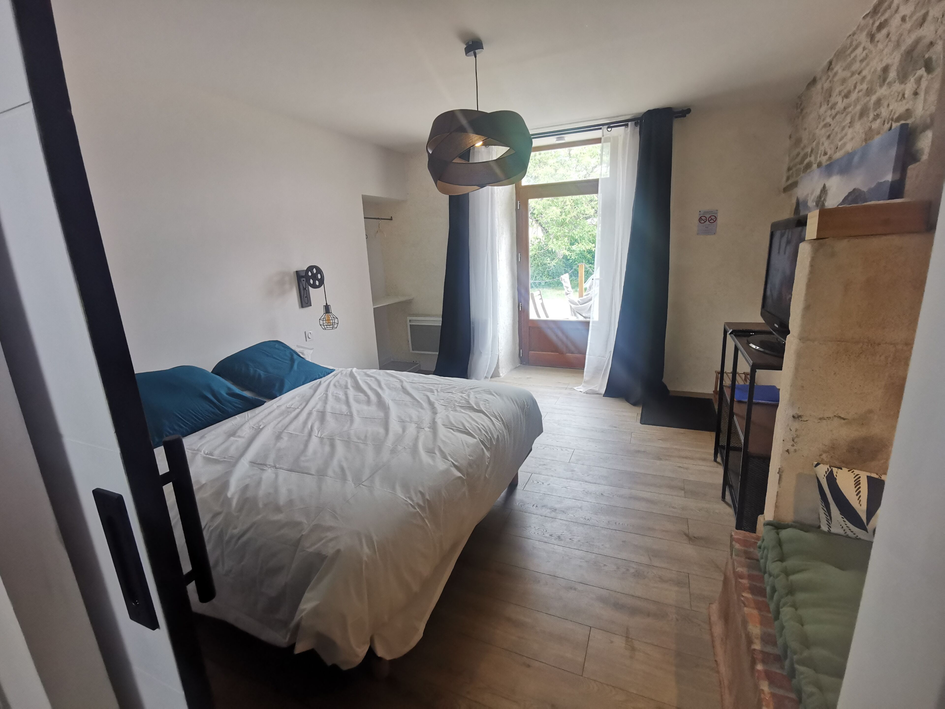Un dormitorio con cama, escritorio, silla, lámpara colgante y vistas al exterior.