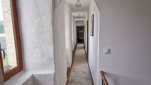 A hallway with a wooden floor, white walls, and a window on the left.