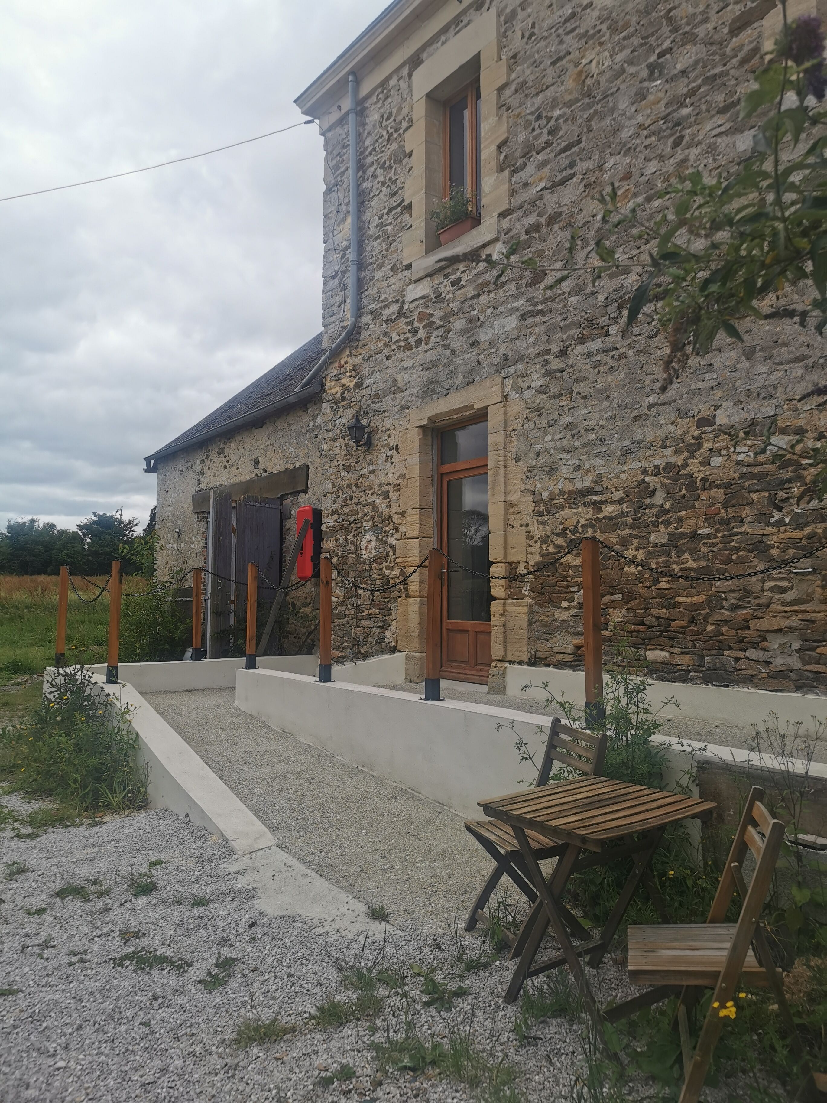 Un bâtiment en pierre avec une porte en bois, une petite fenêtre et un chemin de gravier menant à un banc en bois.