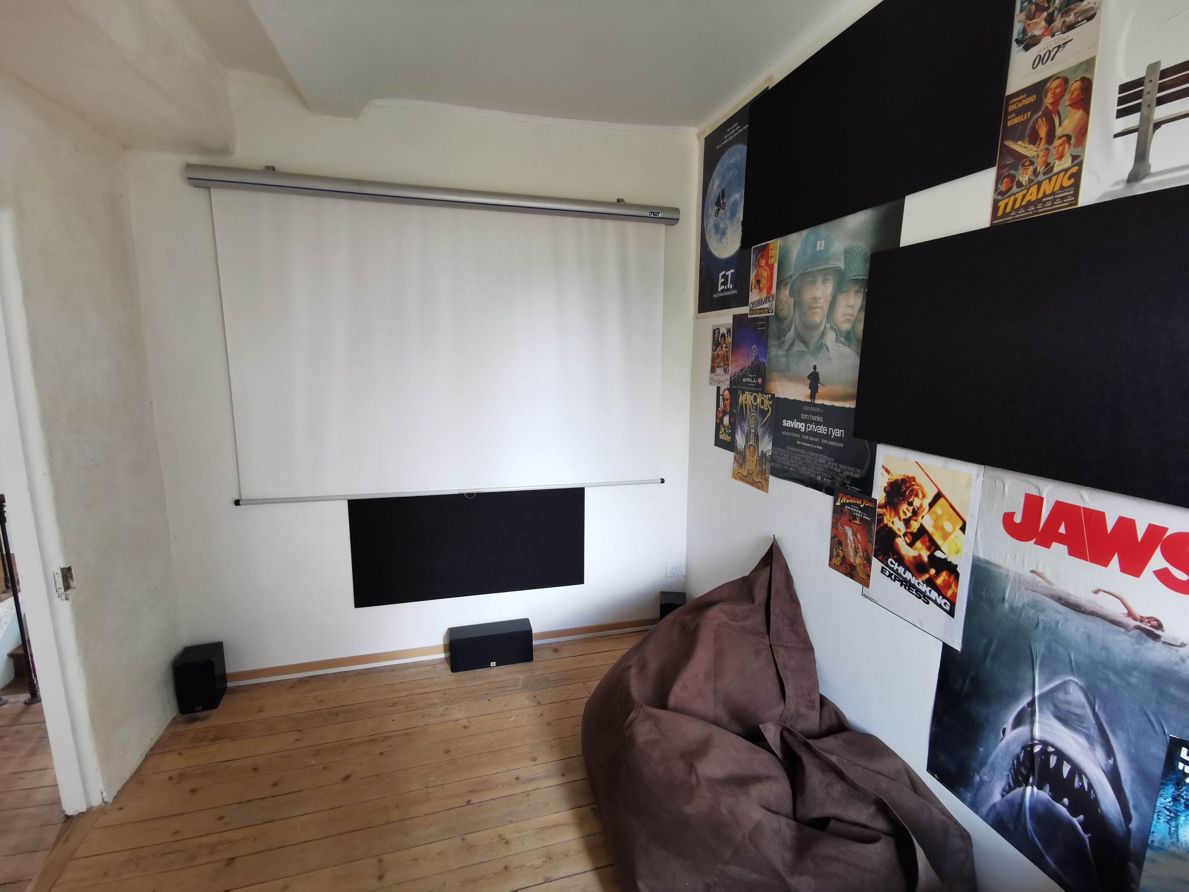 Une pièce avec un plafond blanc, un haut-parleur noir, un fauteuil en forme de poire de couleur marron et des affiches de films accrochées au mur.