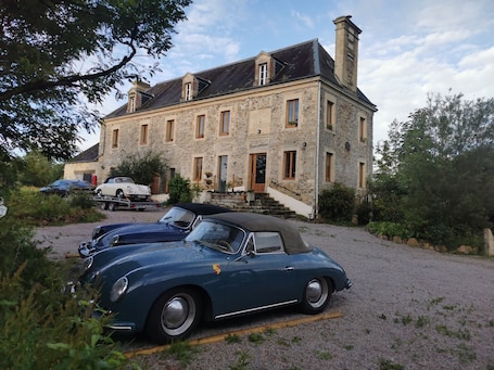 A stone building with a driveway, parked cars, and a staircase leading to the entrance.. Ferme du ru paisible