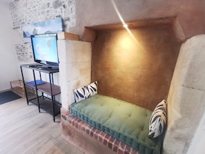 Un rincón acogedor con un banco acolchado, un televisor sobre un mueble y una pared de piedra.
