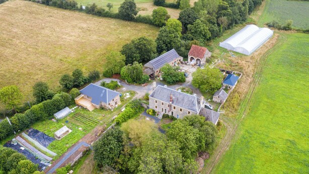 An aerial view of a rural property with multiple buildings, including a house with a sloped roof, a barn, and a greenhouse.