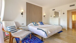 A bedroom with a bed, a chair, a nightstand, a wall-mounted lamp, a mirror, and a patterned rug. - Luxury 2BR Resort Apt, Pools, Spa, Tennis (Estepona)