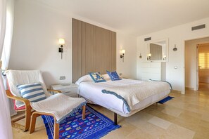 A bedroom with a bed, a chair, a nightstand, a wall-mounted lamp, a mirror, and a patterned rug. - Luxury 2BR Resort Apt, Pools, Spa, Tennis (Estepona)