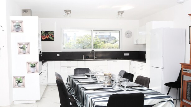 A modern kitchen with white cabinets, a black countertop, and a dining area set for six.