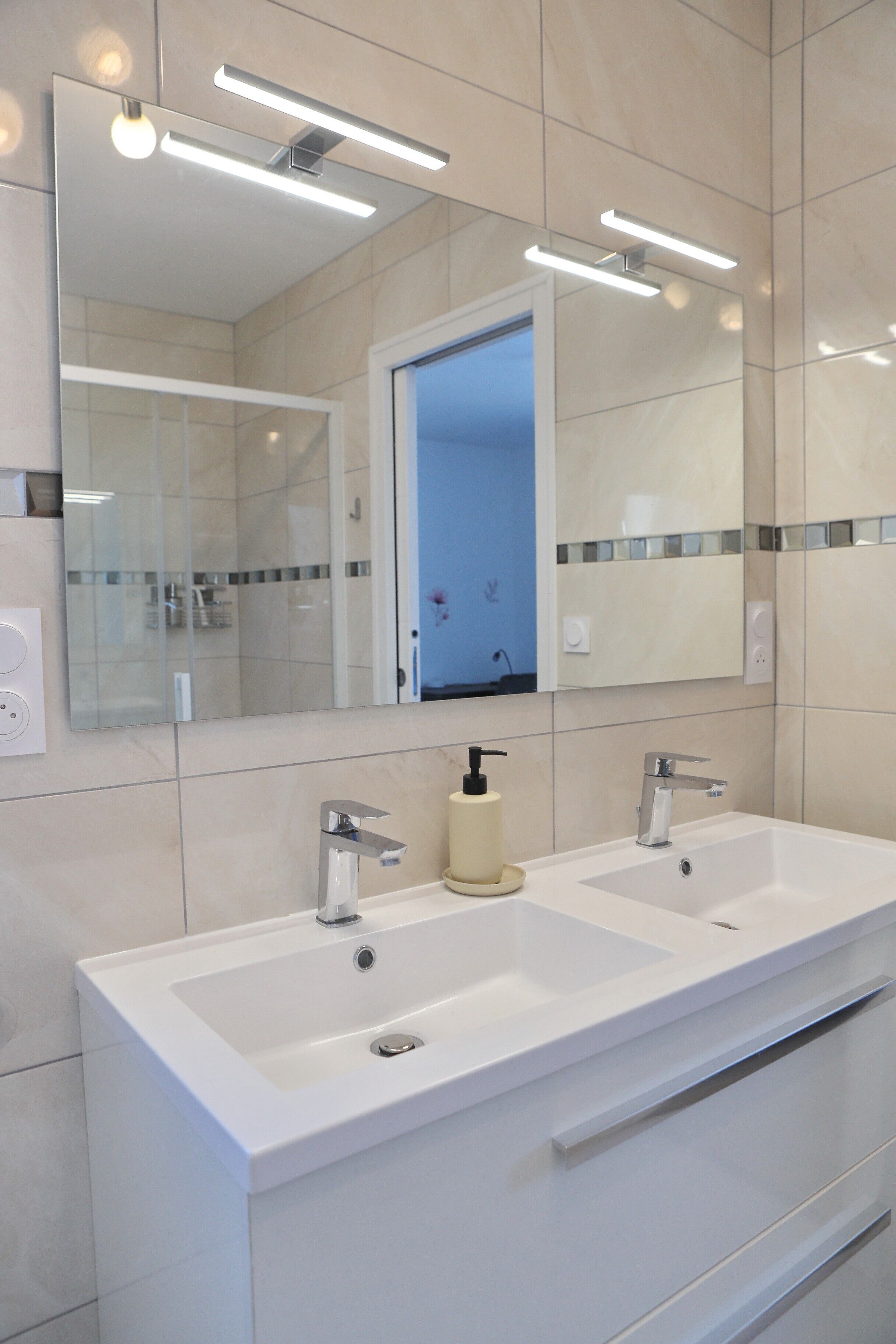 A modern bathroom with two sinks, a large mirror, and overhead lighting.