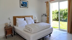 A hotel room with a bed, a nightstand, a lamp, a picture on the wall, and a view of greenery outside.