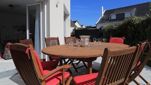 An outdoor dining area with a round wooden table and six wooden chairs with red cushions.