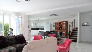 A spacious living area with a sofa, chairs, a dining table, and a staircase leading to another level.