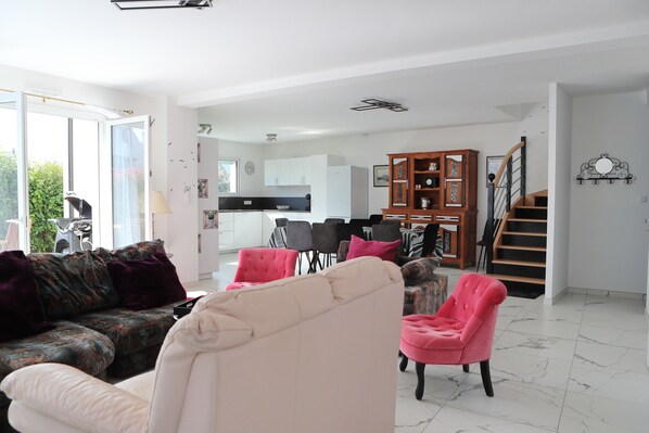 A spacious living area with a sofa, chairs, a dining table, and a staircase leading to another level.