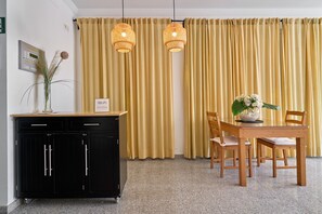 A room with a black cabinet, a wooden table with chairs, yellow curtains, and two wicker pendant lights. - Apartment '2D - 2 Bedrooms 4-6 Guests' with Shared Pool, Wi-Fi, and Air Conditioning (Nerja)