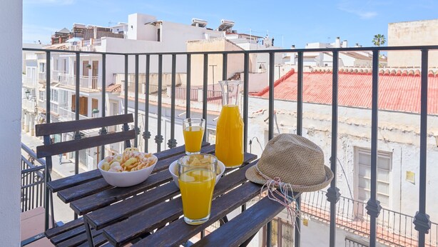 A balcony with a table set for breakfast, including a bowl of snacks, glasses of orange juice, and a bottle of juice. - Apartment '2D - 2 Bedrooms 4-6 Guests' with Shared Pool, Wi-Fi, and Air Conditioning (Nerja)
