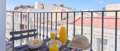 Un balcon avec une table préparée pour le petit-déjeuner, comprenant un bol de collations, des verres de jus d’orange et une bouteille de jus.
