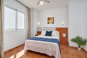 A bedroom with a bed, a nightstand, a wall-mounted telephone, a potted plant, and a window with curtains. - Apartment '2D - 2 Bedrooms 4-6 Guests' with Shared Pool, Wi-Fi, and Air Conditioning (Nerja)