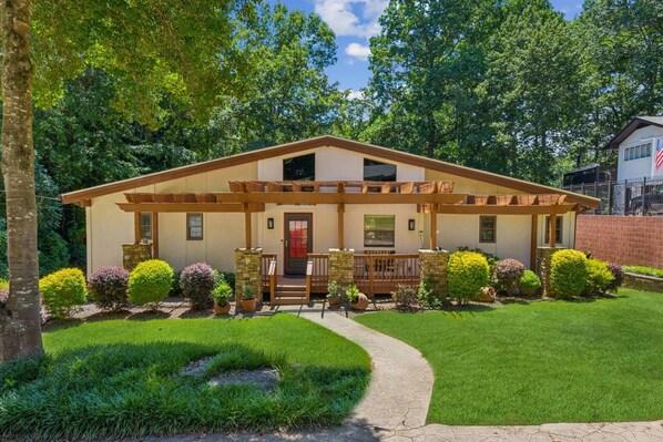 A two-story house with a porch, a front door, and a small garden with potted plants.