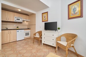 A compact kitchen with a microwave, oven, and white dishwasher. There are wicker chairs and a flat-screen TV on a white cabinet. - Apartment 'P1 Duplex for 2-4 Guests' with Shared Pool, Wi-Fi and Air Conditioning (Nerja)