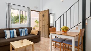 A living room with a sofa, a coffee table, a dining table with chairs, a staircase, and a door leading outside. - Apartment 'P1 Duplex for 2-4 Guests' with Shared Pool, Wi-Fi and Air Conditioning (Nerja)