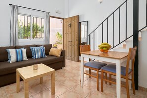 A living room with a sofa, a small table, a dining table with chairs, a staircase, and a door leading to an outdoor area. - Apartment 'P1 Duplex for 2-4 Guests' with Shared Pool, Wi-Fi and Air Conditioning (Nerja)