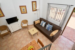 A living room with a sofa, chairs, a TV, a table with fruit, and a window with a view. - Apartment 'P1 Duplex for 2-4 Guests' with Shared Pool, Wi-Fi and Air Conditioning (Nerja)