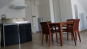 Une cuisine compacte équipée d’un réfrigérateur, d’une cuisinière et d’un four à micro-ondes. On y trouve une table à manger avec quatre chaises. La pièce a des murs blancs et un plafond en pente.