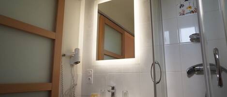 A bathroom with a white sink, a mirror, a shower with a glass door, and a tiled wall.